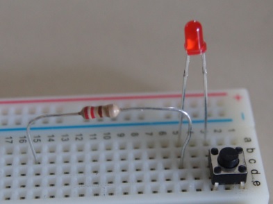 Detail of a breadboard with a button, resistor and an LED in a circuit