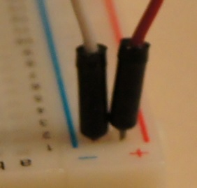 Detail of jumper wires connected to the positive and negative busses on a breadboard