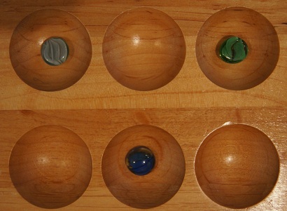 Mancala board with one stone in the first pocket and one stone in the third pocket on the first row and one stone in the second pocket on the second row.