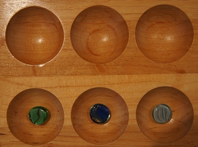Mancala board with no stones in the first row and one stone in each of the first three pockets on the second row.